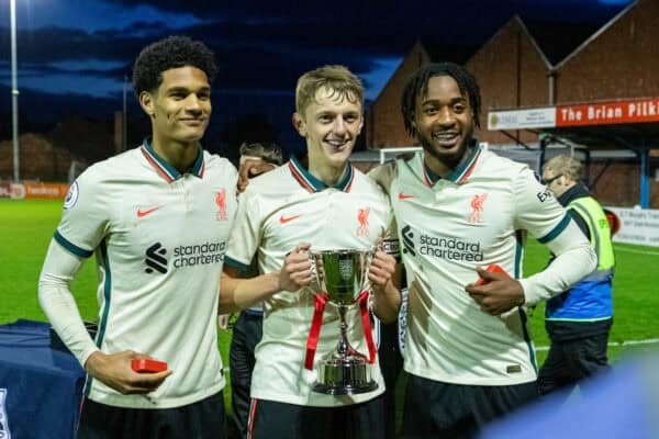 Liverpool football players celebrating with trophy on the pitch after match victory.