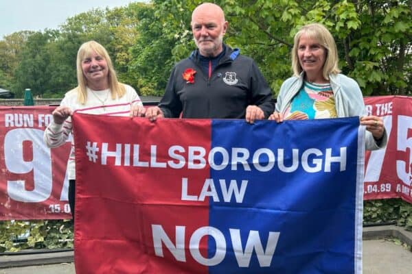 Margaret Aspinall- mother of James Aspinall, Steve Kelly - brother of Michael Kelly, Sue Roberts - sister of Graham Roberts hold Hillsborough Law Now banner - May 18, 2023
